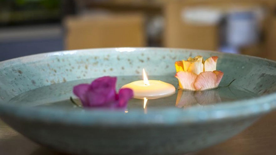 Eine brennende Kerze und zwei Blumen schwimmen in einer Keramik-Schüssel mit Wasser