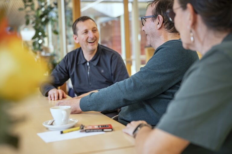 Fröhlicher Austausch zwischen 3 Personen, die am Tisch sitzen
