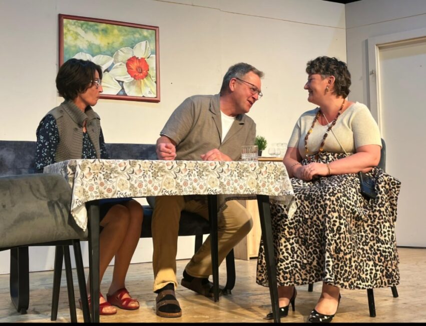 Zwei Frauen in der Mitte ein man diskutieren am Tisch auf der Bühne des Theaters