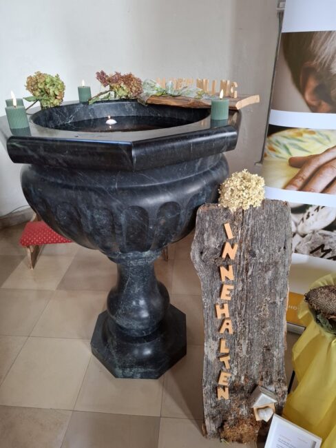 Ein mit Wasser gefüllter Taufstein auf dem Kerzen stehen