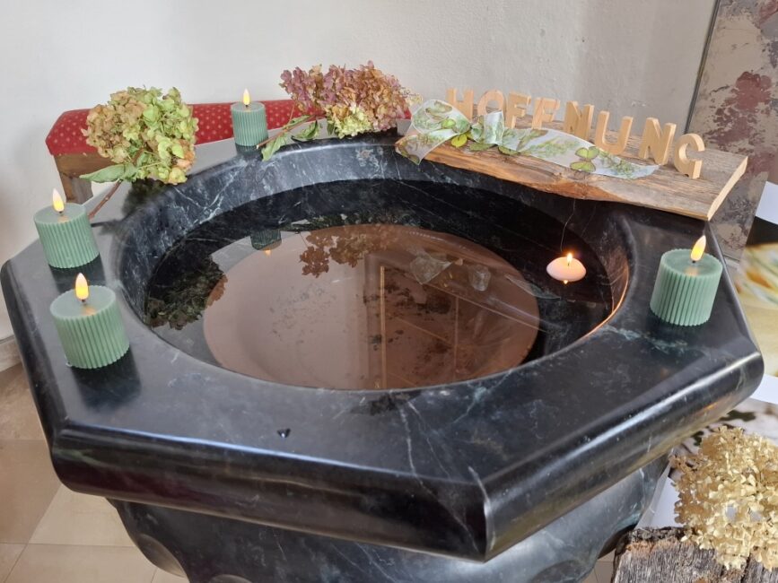 Taufbecken mit Kerzen und Holzbuchstaben die das Wort Hoffnung bilden