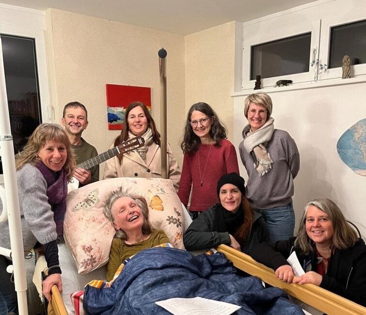 Mitarbeiter*innen beim "Anklöpfeln" stehen am Bett einer Patientin