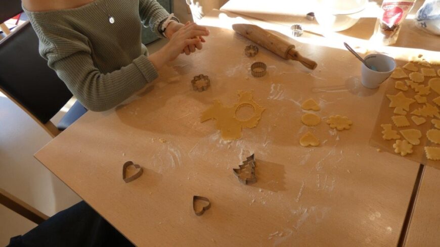 Ein Kind hält Teig in der Hand, am Tisch liegen Kekse und Austechformen