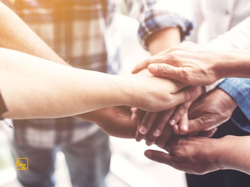 Mehrere Hände von verschiedenen Personen liegen als Zeichen von Gemeinschaft und Zusammenhalt übereinander.
