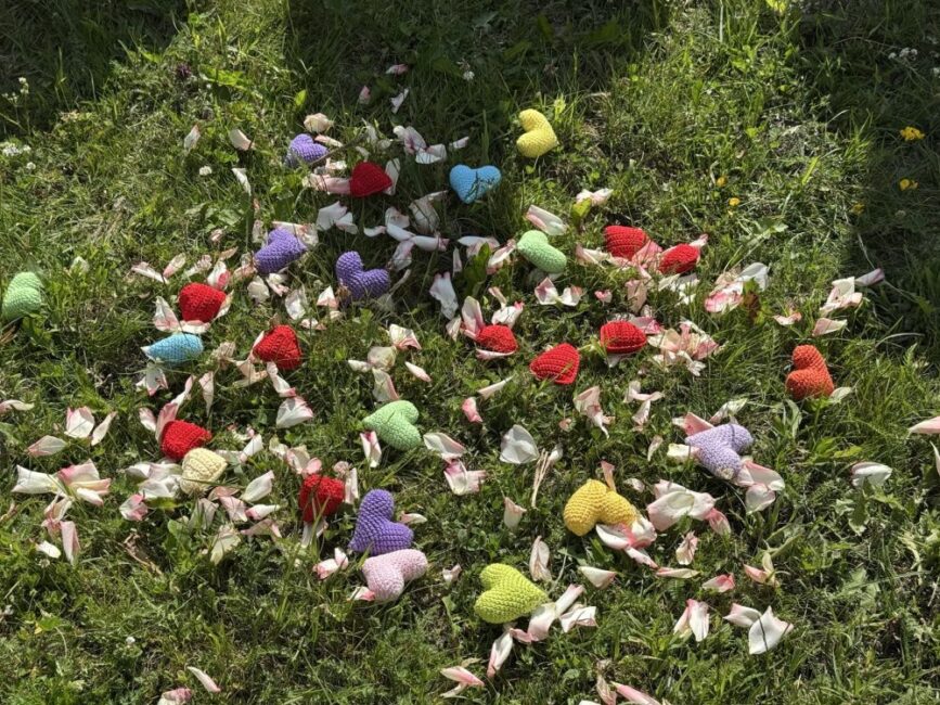 Viele gehäkelte Herzen liegen auf der grünen Wiese mit Bumenblättern