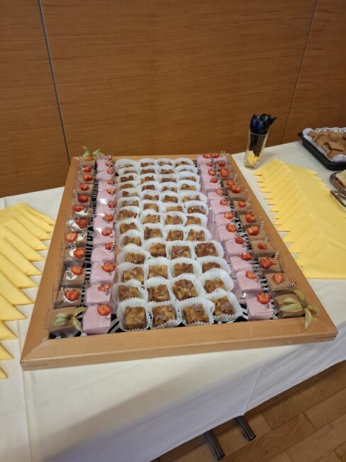 Ein großes Holztablett auf einem Buffet mit nett angerichteten Nachspeisen, kleinen Kuchenstücken und Dessertgläsern mit Erdbeeren