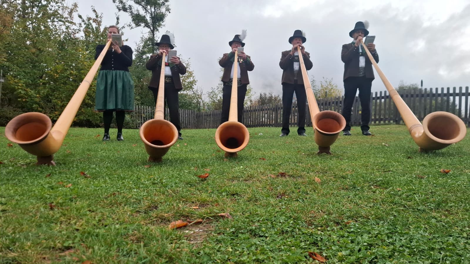 Fünf Personen in Tracht spielen im Freien auf Rasen Alphorn.