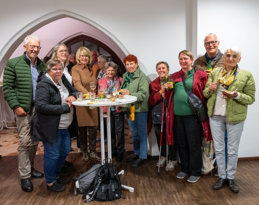 Eine Gruppe von Gottesdienstbesuchenden steht lächelnd zusammen um einen Stehtisch bei einem Umtrunk mit Getränken und kleinen Häppchen.