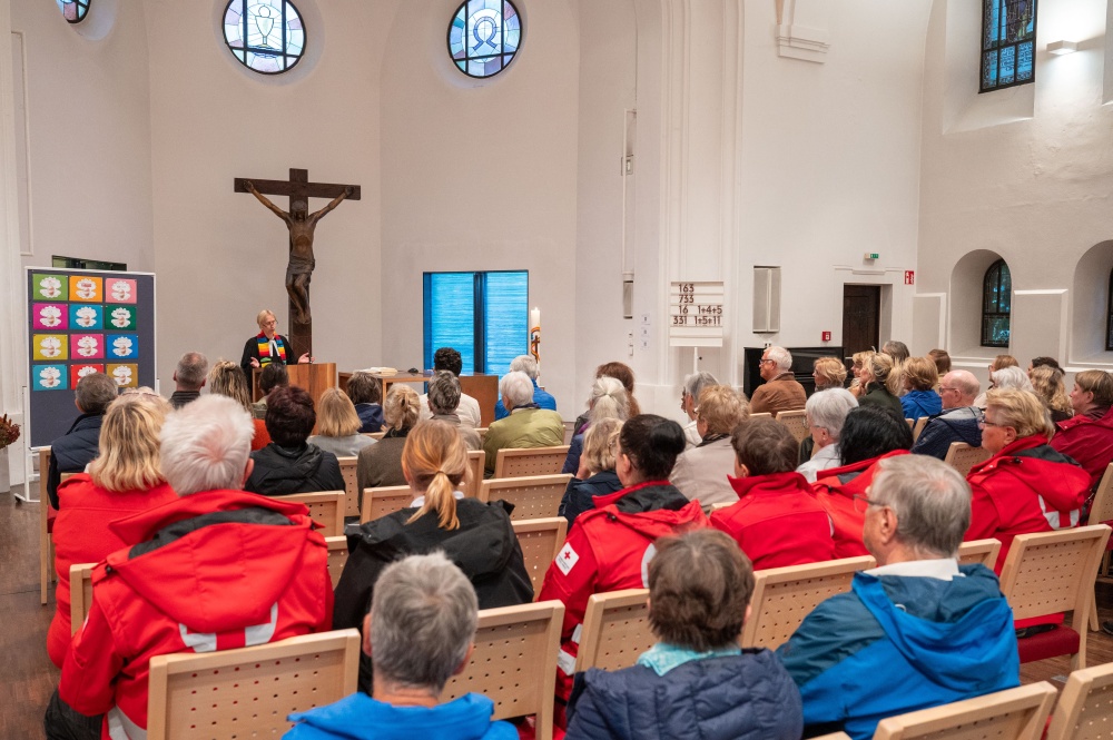Blick von hinten auf die gut gefüllten Stuhlreihen einer Kirche während einer Predigt der Pfarrerin am Altar.