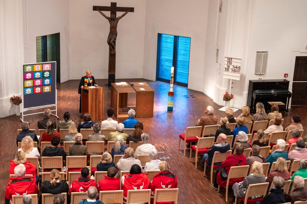 Blick von oben auf den Altarraum einer Kirche während einer Predigt der Pfarrerin vor der sitzenden Gemeinde.