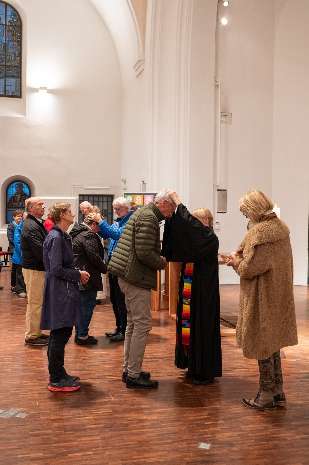 Eine Pfarrerin legt einem Mann bei einer Segnung in einer Kirche die Hand auf den Kopf, während andere Menschen in einer Reihe warten.